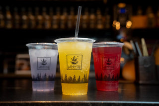 Three drinks with different colored liquids on a bar counter, featuring brand logos.